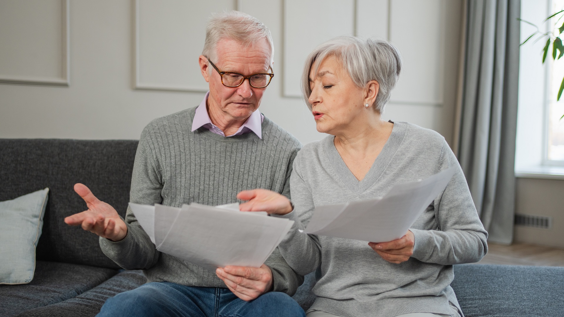 Sad tired disappointed middle aged senior couple sit with paper document. Unhappy older mature man woman reading paper bill managing bank finances calculating taxes planning loan debt pension payment. stock photo